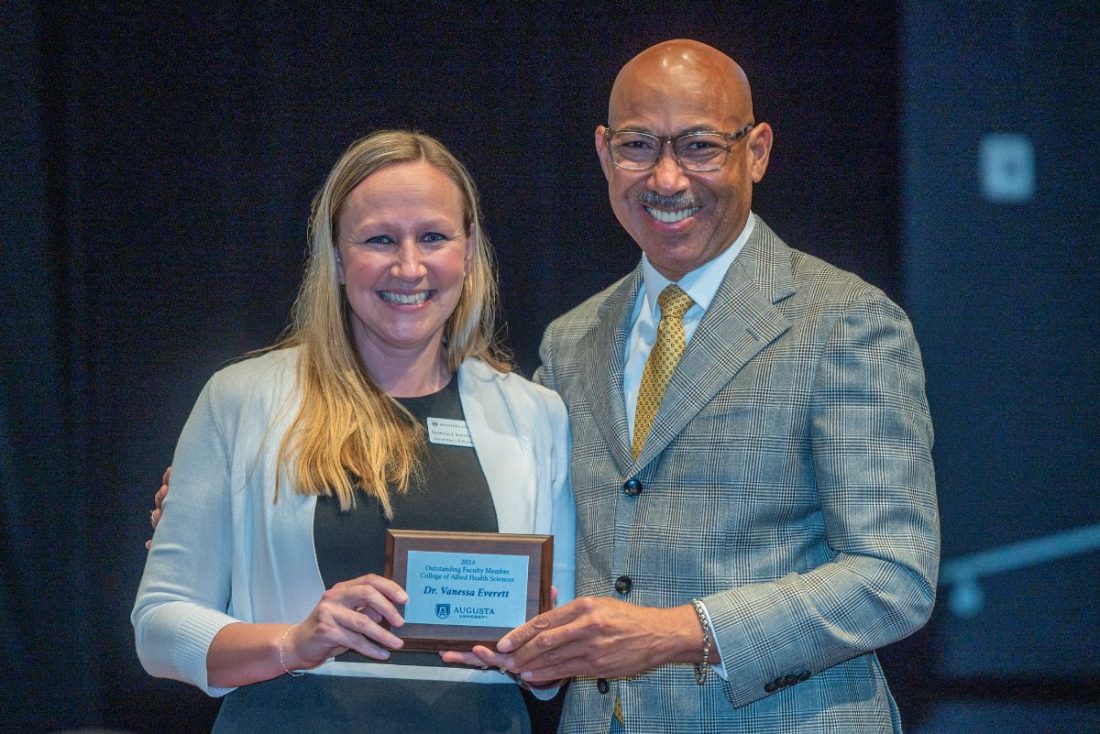 A woman holds up an award plaque while standing next to a man.