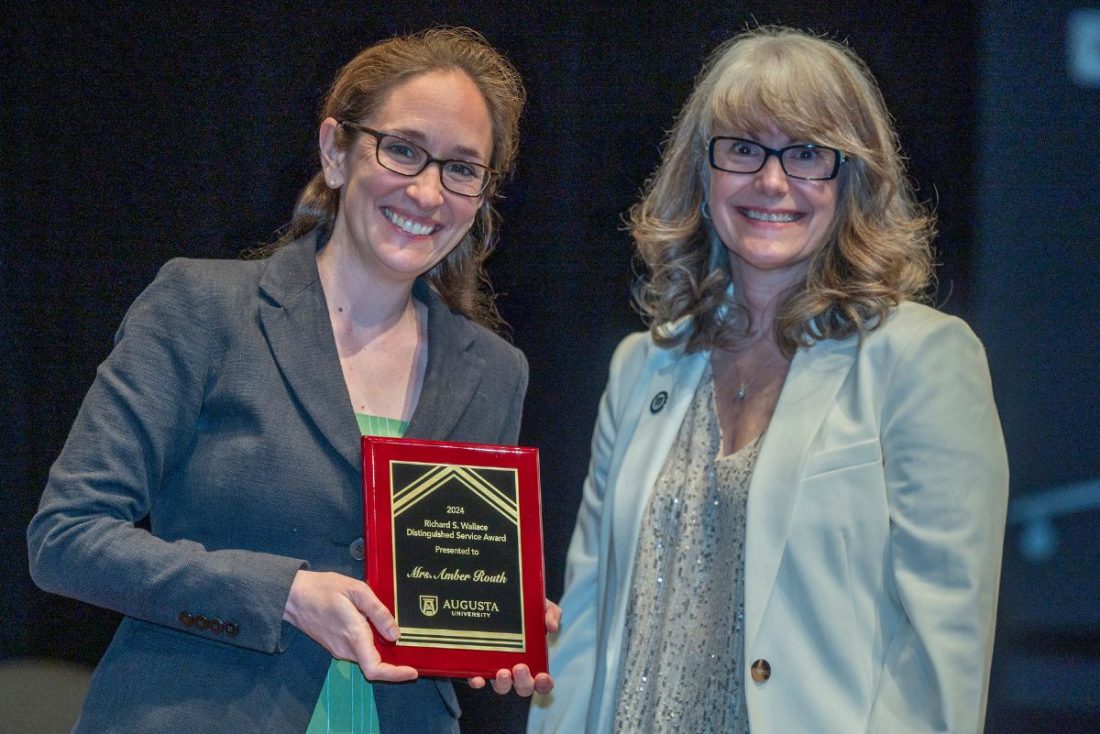 Two women stand together as one holds up an award plaque.