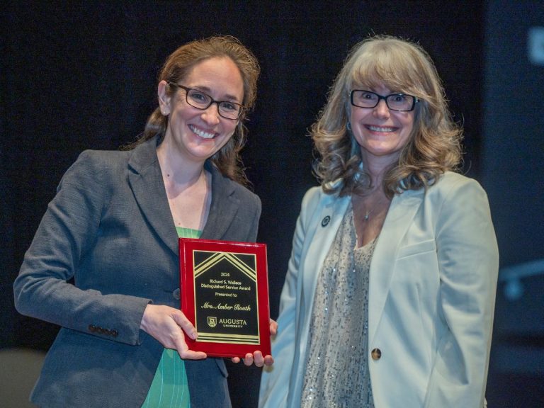 Two women stand together as one holds up an award plaque.