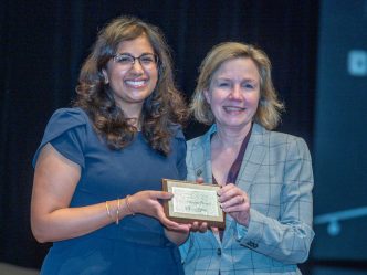 Two women hold an award while smiling at the camera