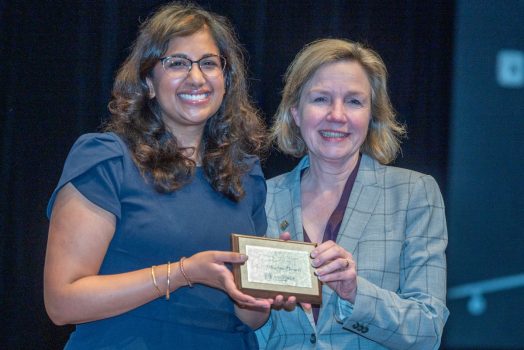 Two women hold an award while smiling at the camera