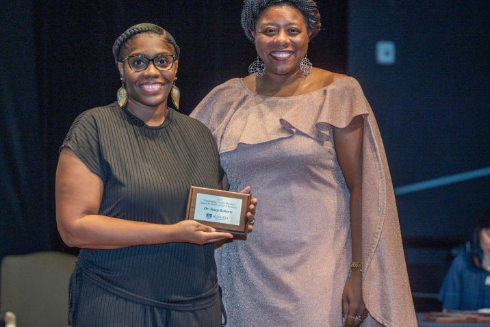 two women smile at the camera while the woman on the left holds an award