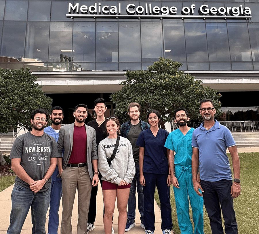 Seven medical students and two medical instructors pose and smile in front of the Medical College of Georgia building.