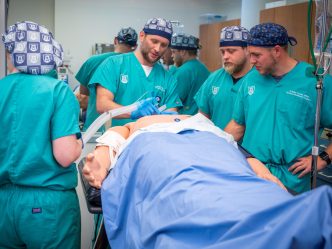 Anesthesia students in teal scrubs learn to intubate on a simulation model