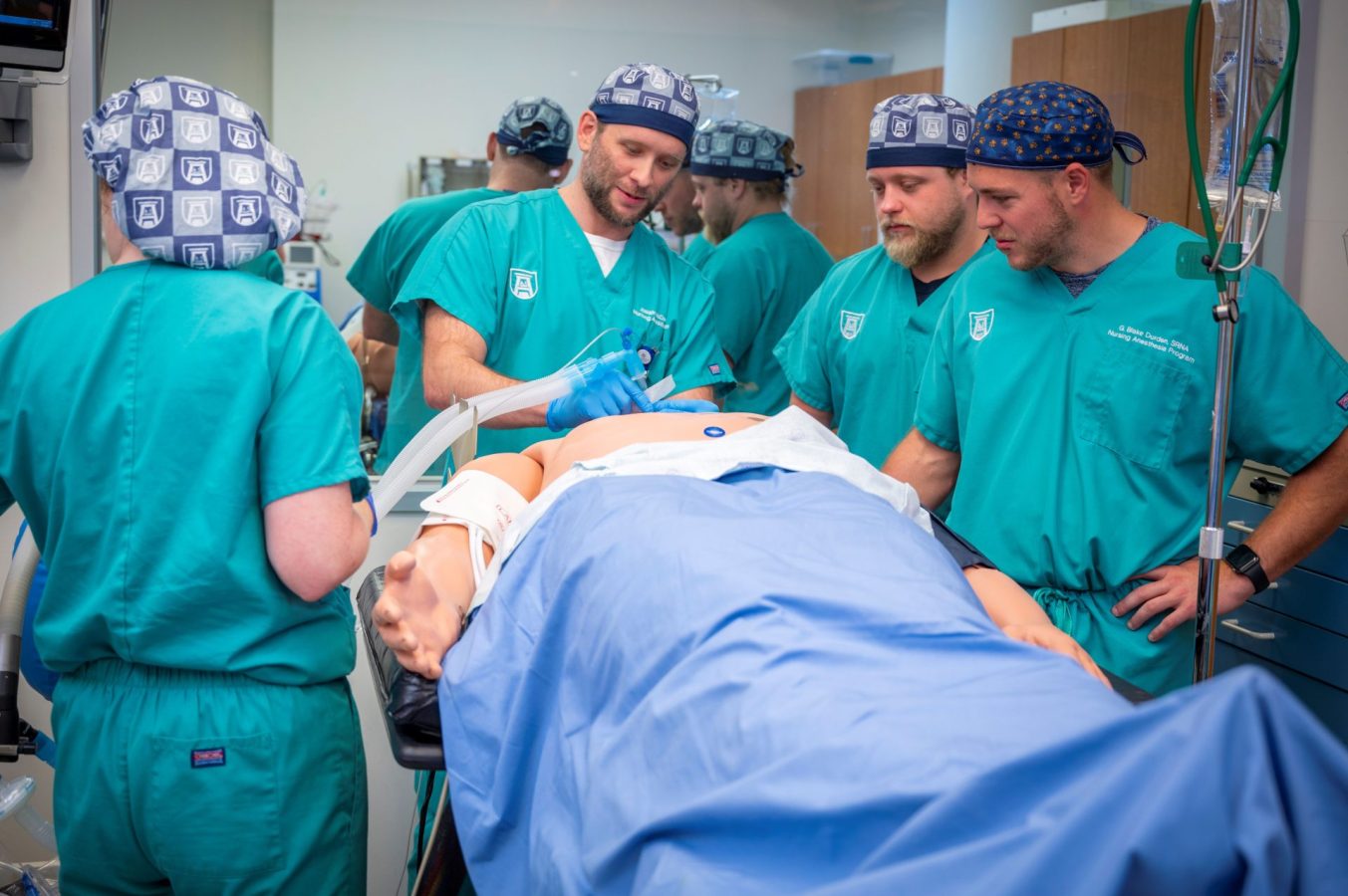 Anesthesia students in teal scrubs learn to intubate on a simulation model