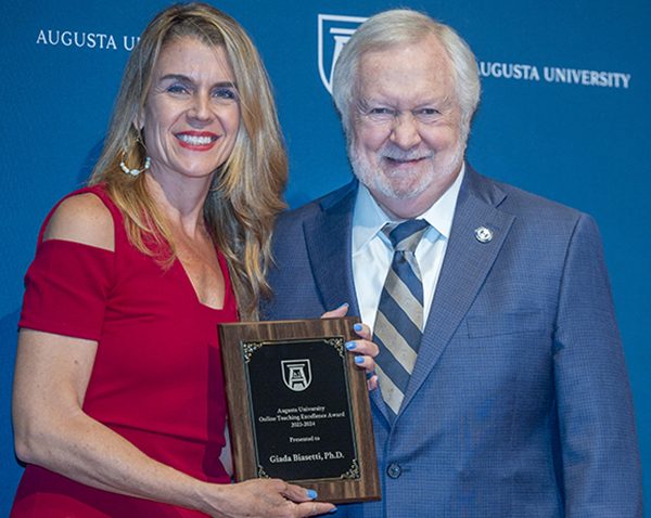 A man and woman hold up an award plaque together.