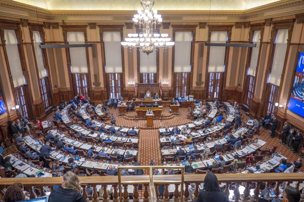 A chamber inside a state capitol building with legislators sitting at their desks.