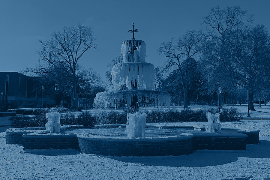 A fountain is frozen with snow all around on the ground around it.