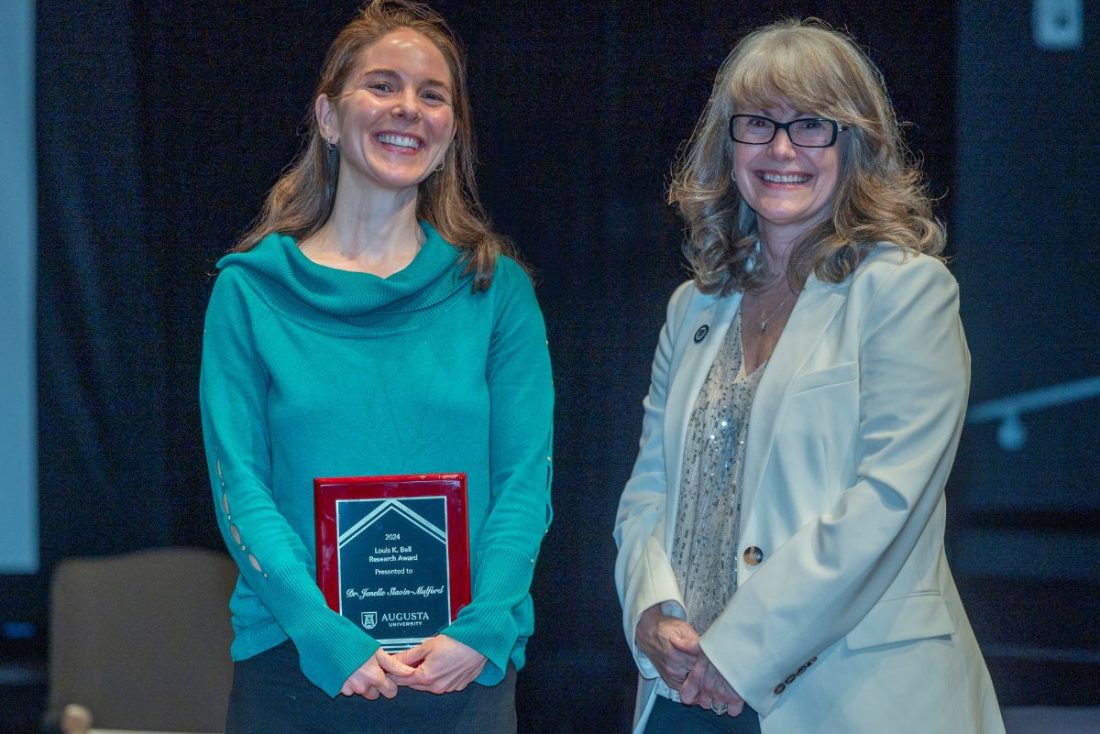 Two women stand together. One is holding a plaque.