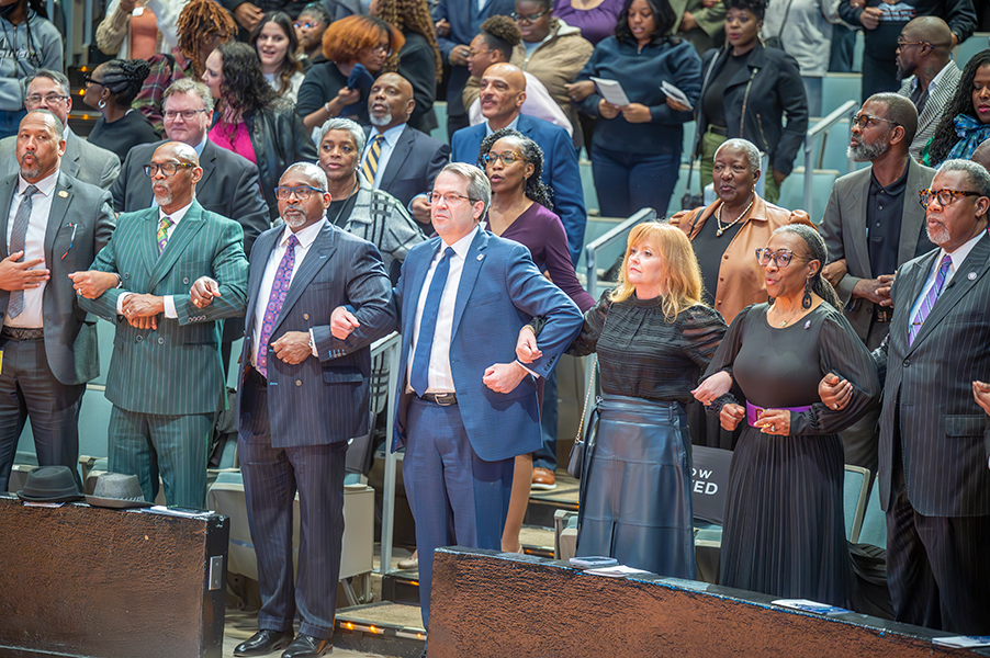 Members of a crowd lock arms in solidarity and sing a song at the 2025 Rev. Dr. Martin Luther King Jr. Tri-College Celebration.
