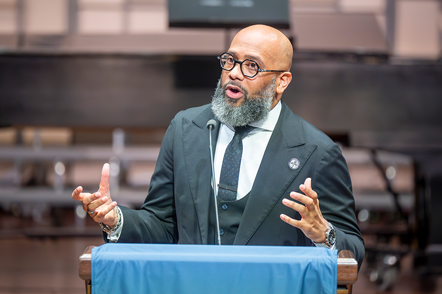 A man in a suit speaks standing behind a lectern.