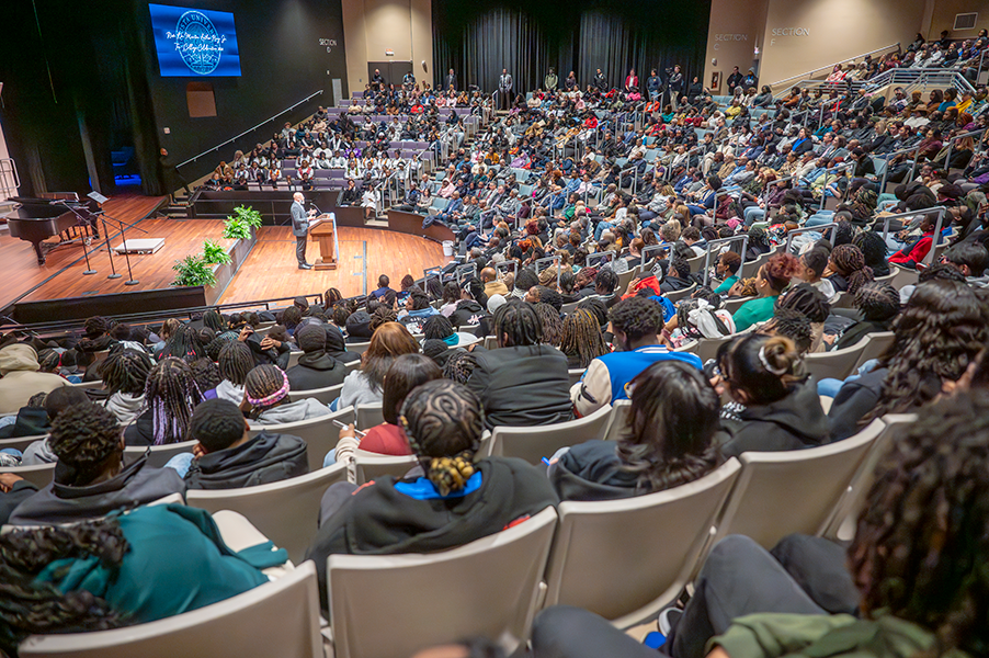 Speaker at a lectern, while most seat in a theater are filled.