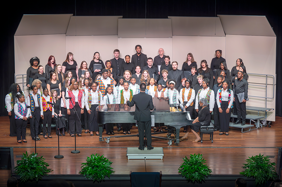 A large choir with young people singing on stage with a piano.