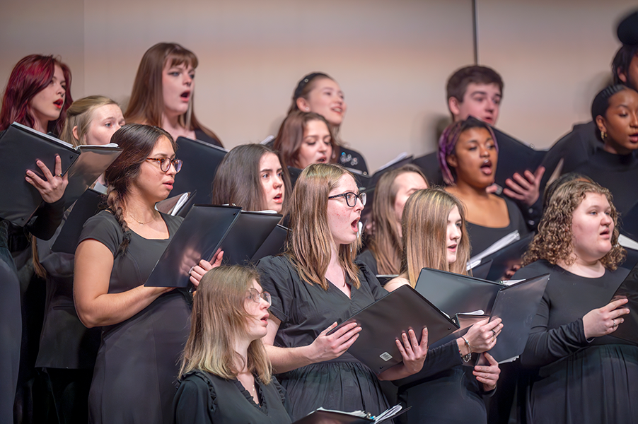 Young adults hold music books and sing a song.