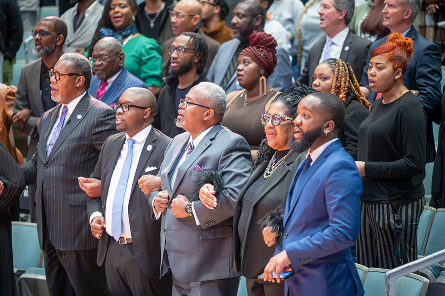 Members of a crowd lock arms in solidarity and sing a song at the 2025 Rev. Dr. Martin Luther King Jr. Tri-College Celebration.
