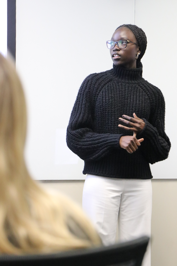 A female college student stands at the front of a classroom and presents to her class.