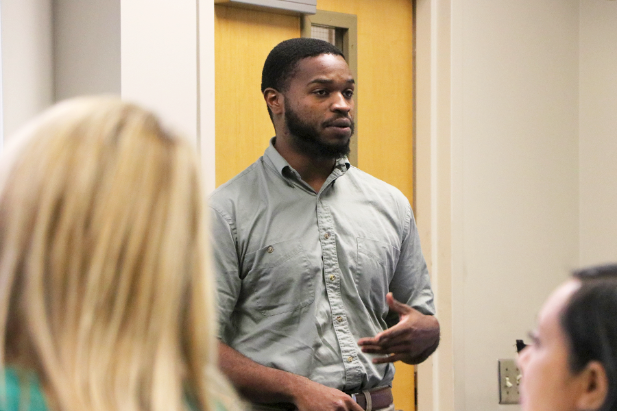 A male college student stands at the front of a classroom and presents to his class.