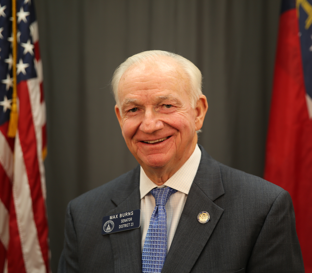 Man in a suit standing in front of a United States flag and the Georgia state flag