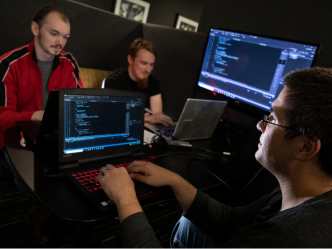 College students studying cybersecurity work on laptops in a computer lab.