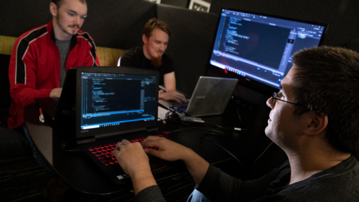 College students studying cybersecurity work on laptops in a computer lab.