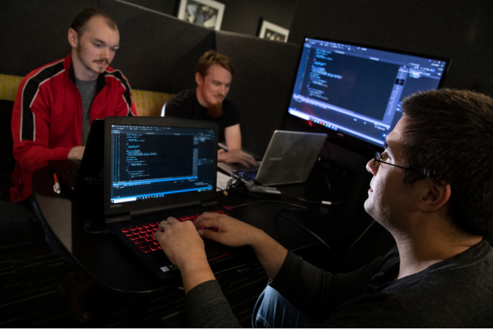 College students studying cybersecurity work on laptops in a computer lab.