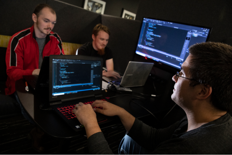 College students studying cybersecurity work on laptops in a computer lab.