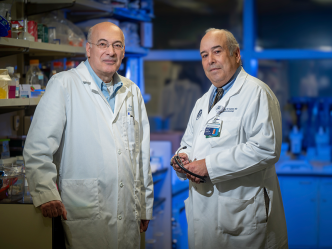 Two male scientists stand in a lab. Both are wearing lab coats.