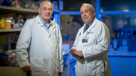 Two male scientists stand in a lab. Both are wearing lab coats.