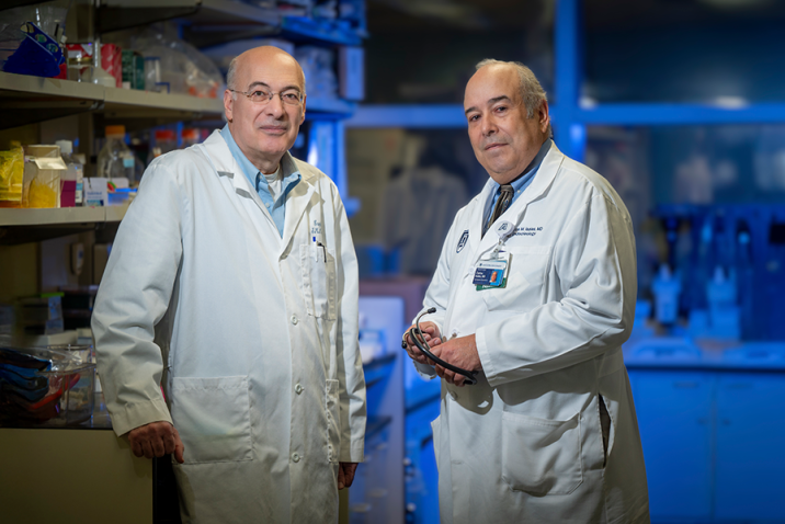 Two male scientists stand in a lab. Both are wearing lab coats.