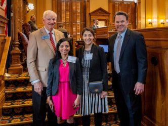 Four people stand in a large room in a government capitol building.