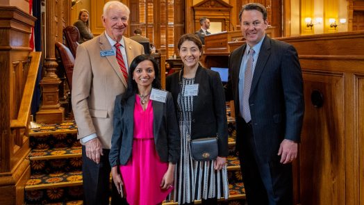 Four people stand in a large room in a government capitol building.