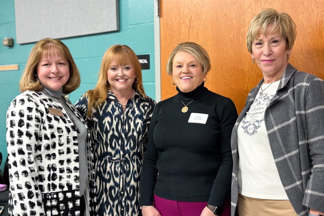 Four women stand in a classroom.