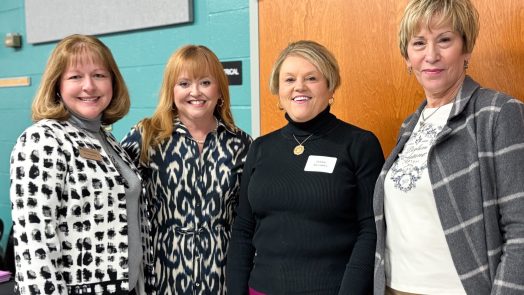 Four women stand in a classroom.