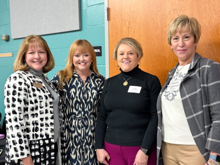 Four women stand in a classroom.