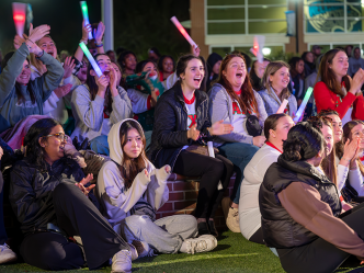 College students sit around an outdoor amphitheater and cheer during a Homecoming event.