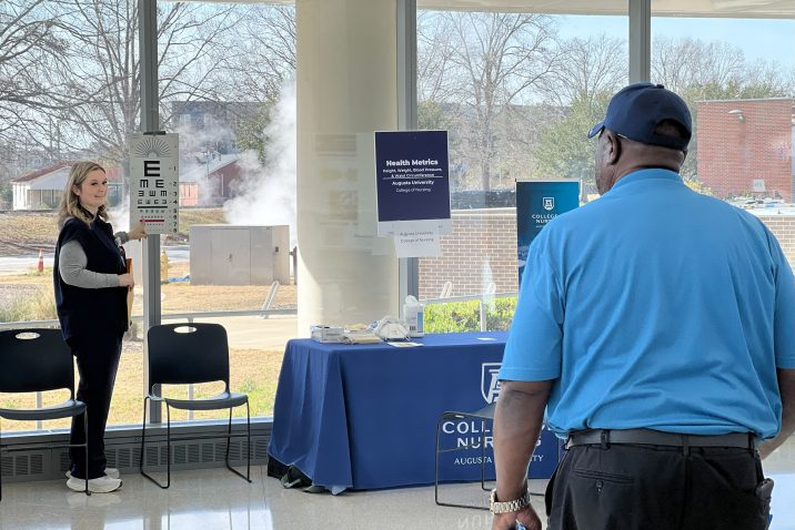 A college student studying to become a nurse conducts a vision exam for a man during a health fair in a large lobby.