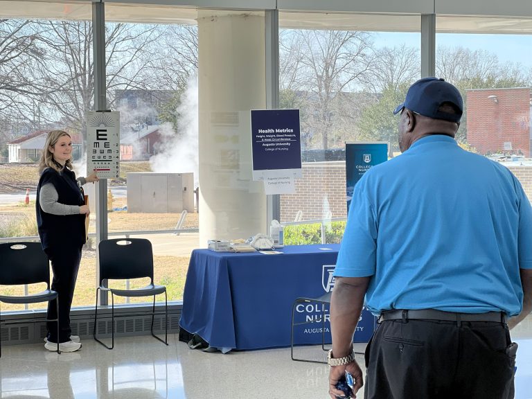 A college student studying to become a nurse conducts a vision exam for a man during a health fair in a large lobby.