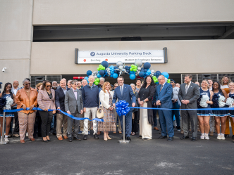 A large group of people stands behind a ribbon after it is cut. They are in front of ballons.