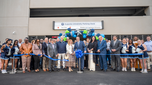 A large group of people stands behind a ribbon after it is cut. They are in front of ballons.