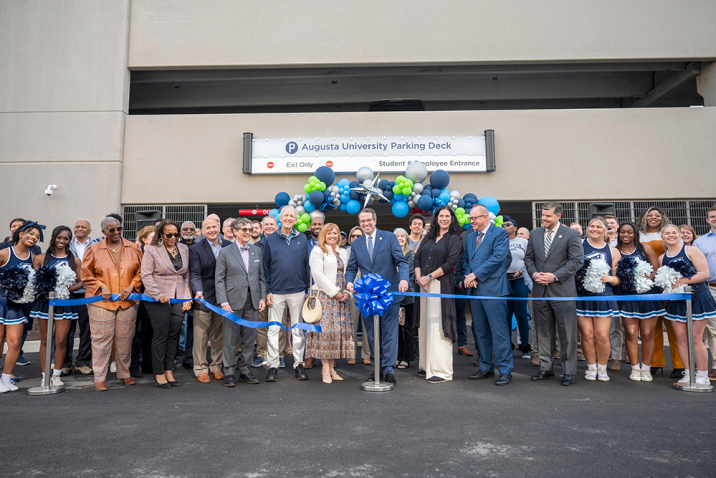 A large group of people stands behind a ribbon after it is cut. They are in front of ballons.