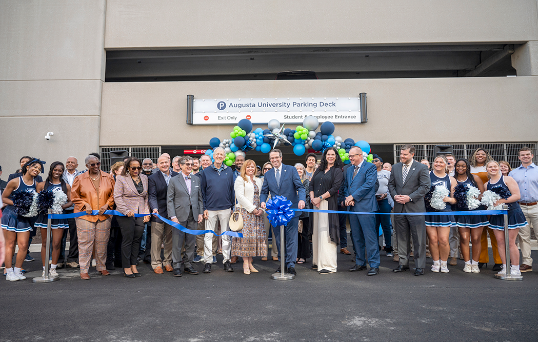 A large group of people stands behind a ribbon after it is cut. They are in front of ballons.