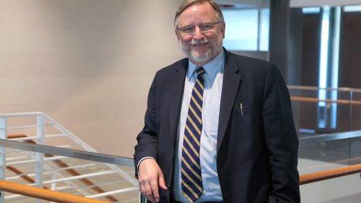A man in a suit and tie stands in a large atrium and leans against a railing.