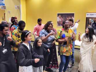 A group of people gather in a large atrium and dance as music plays.