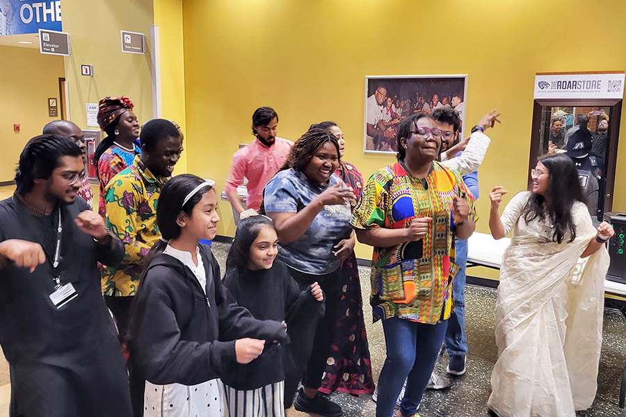 A group of people gather in a large atrium and dance as music plays.