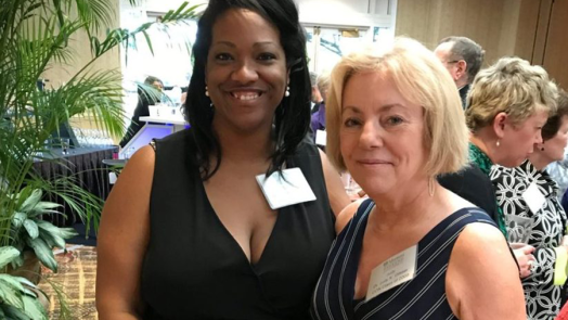 Two women stand in a large banquet room.