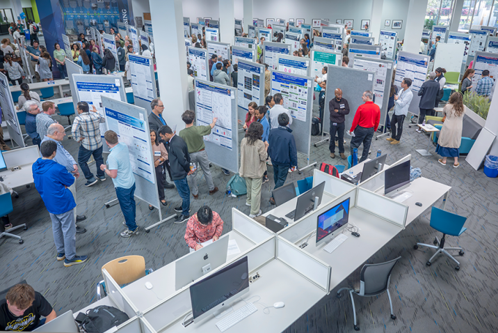 View from above looking down at young adults and visitors looking at large presentation boards in crowded room