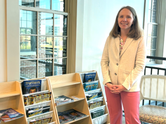 A woman stands next to bookshelves filled with children's books.