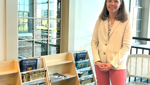 A woman stands next to bookshelves filled with children's books.