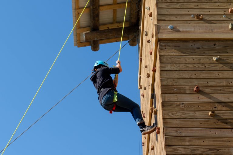 An Augusta University student hanging from a rope climbs a rock wall.
