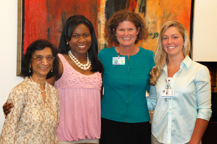 Four women stand together in front of a large painting.